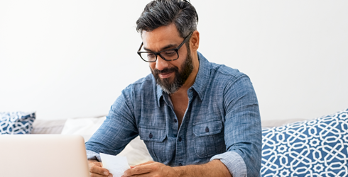 man in glasses looking at paper on laptop