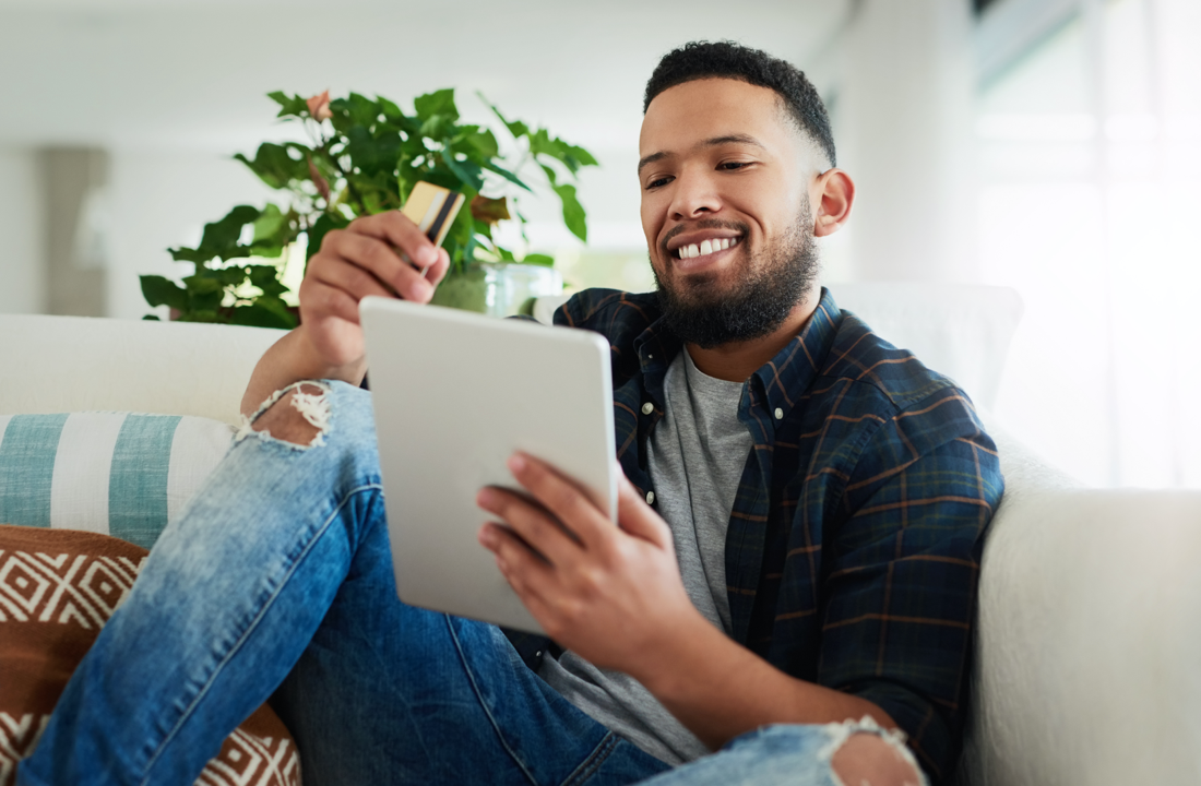 man smiling with credit card and tablet on couch